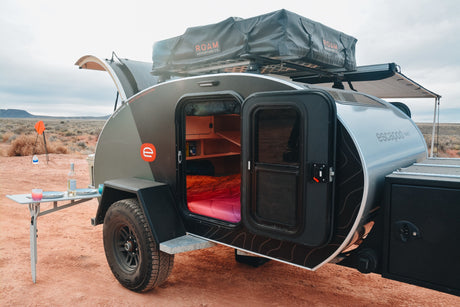 This Escapade teardrop camper, an ideal RV rental, offers adventure with its rooftop tent & outdoor setup in the desert.