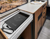 Inside an RV rental: a modern, compact kitchen featuring a pull-out True Induction cooktop for easy meals on the go.