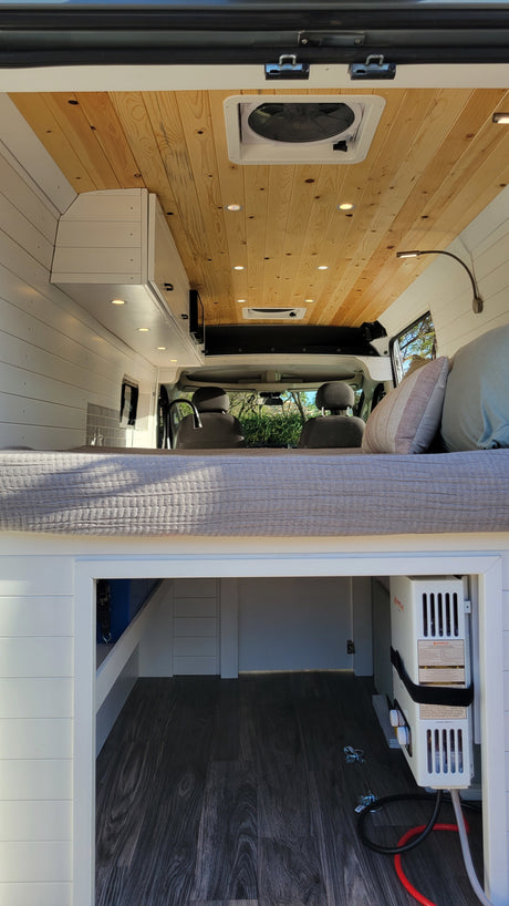 Cozy camper van interior for RV rental: wood ceiling, raised bed, and under-bed storage with water heater.