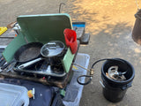 Outdoor cooking at your RV rental: a portable propane stove with a cast iron pan & pot, plus a water jug, on a picnic table.