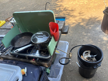 Outdoor cooking at your RV rental: a portable propane stove with a cast iron pan & pot, plus a water jug, on a picnic table.