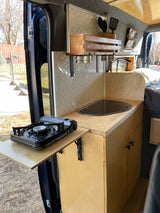 Inside a stylish camper van: organized kitchen area with a pull-out stove, sink, and tiled backsplash, great for rv rental.