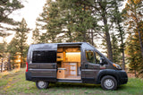 RV rental: a cozy gray camper van with an illuminated interior, parked in a pine forest, bathed in sunset glow.