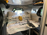 Cozy RV rental interior featuring a bed with "destination camping" bedding, laptop table, and ceiling fan.