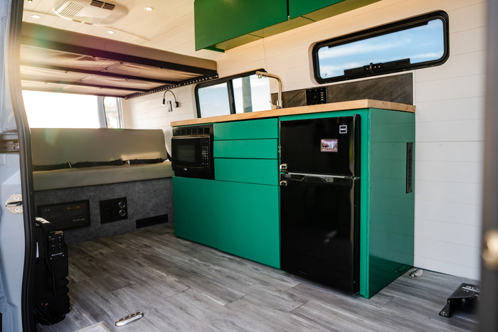 Modern RV rental interior features a vibrant green kitchen with microwave, fridge, sink, and cozy seating.