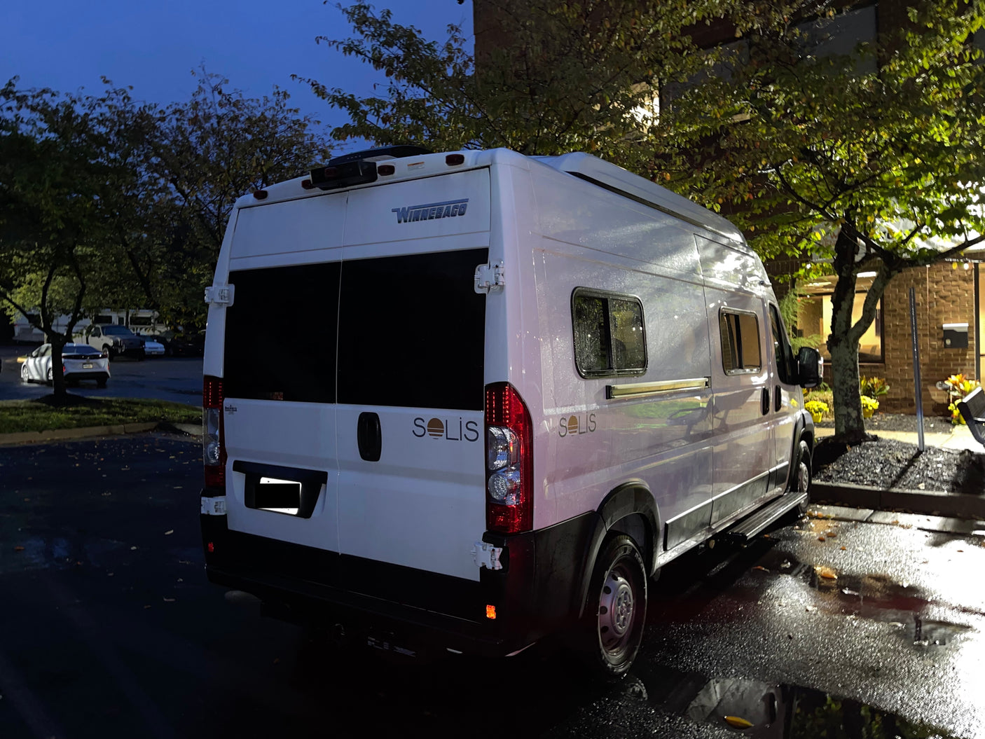 A sleek white Winnebago Solis camper van, perfect for rv rental, parked on wet asphalt at night.