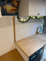 Cozy RV rental kitchenette with wood counter, white subway tile, gold faucet, built-in fridge, and seating area for travel comfort.