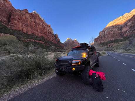 An overlanding truck, great for an RV rental trip, parked on a road with red rock mountains glowing in the sunrise. Climbing rope ready.