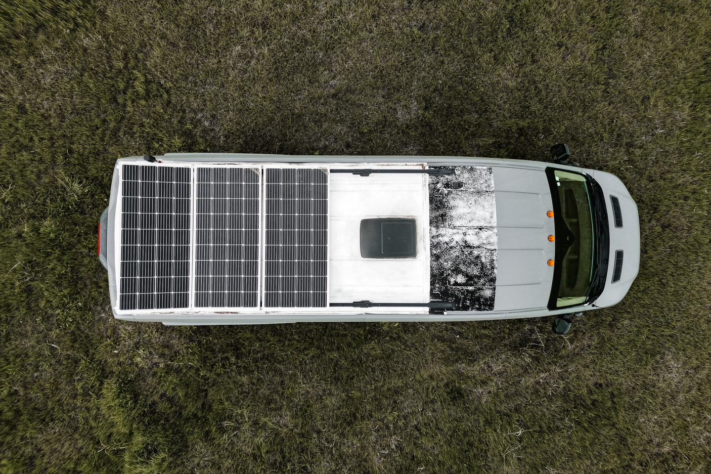 Overhead view of a gray RV rental with rooftop solar panels, parked in a grassy field, ready for off-grid travel.