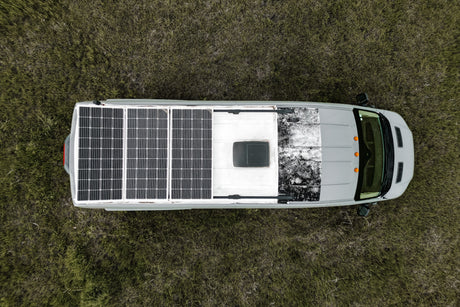 Overhead view of a gray RV rental with rooftop solar panels, parked in a grassy field, ready for off-grid travel.