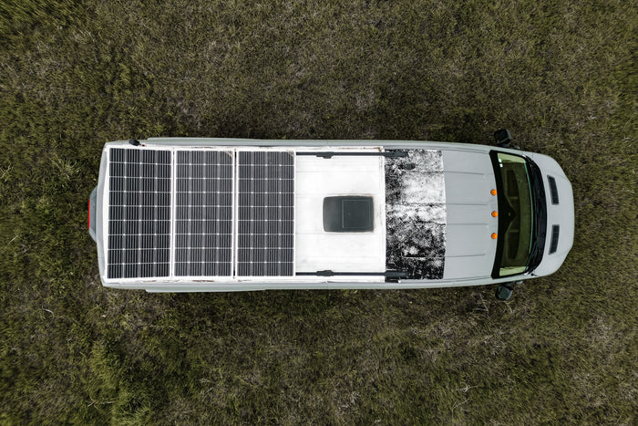 Overhead view of a gray RV rental with rooftop solar panels, parked in a grassy field, ready for off-grid travel.