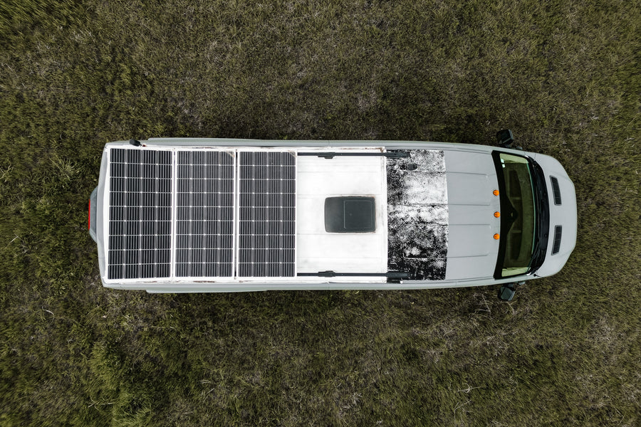 Overhead view of a gray RV rental with rooftop solar panels, parked in a grassy field, ready for off-grid travel.