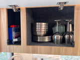 RV rental kitchen cabinets open, revealing a first aid kit, stacked metallic dishes, and stemware, all neatly stored in felt-lined compartments.