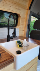 This RV rental's modern kitchen features a sleek black faucet, white farmhouse sink, wood counters, and cozy wood paneling.