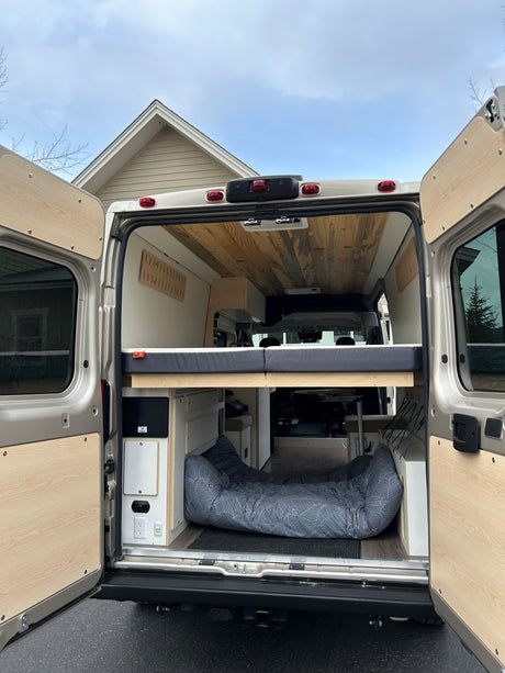 Rear view of an RV rental van conversion: a raised bed, storage, and a dog bed on the floor. Ready for adventures!
