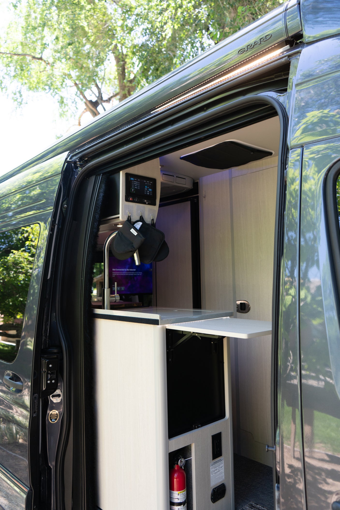 This RV rental shows an open side door, revealing a compact interior kitchen with a sink, controls, and a fold-out table.