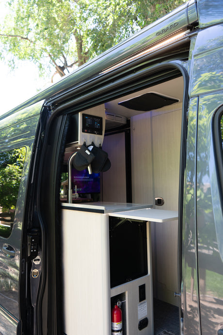 This RV rental shows an open side door, revealing a compact interior kitchen with a sink, controls, and a fold-out table.