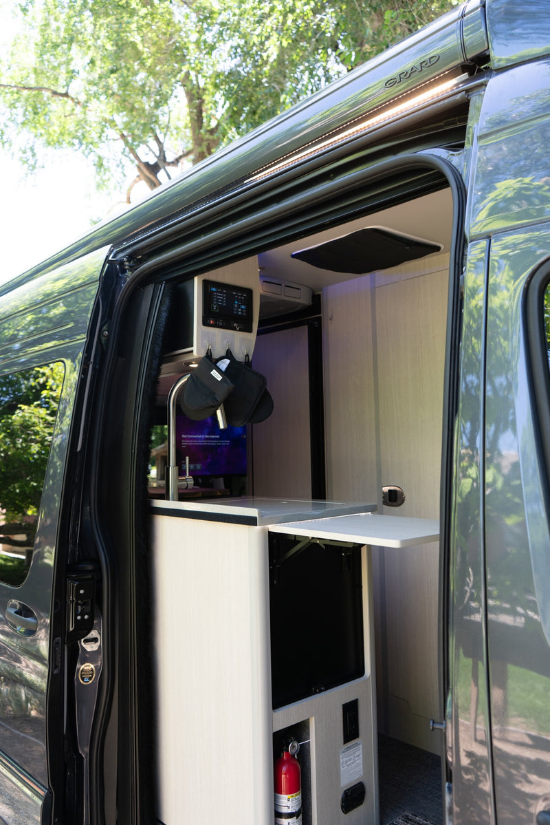 This RV rental shows an open side door, revealing a compact interior kitchen with a sink, controls, and a fold-out table. — photo 2