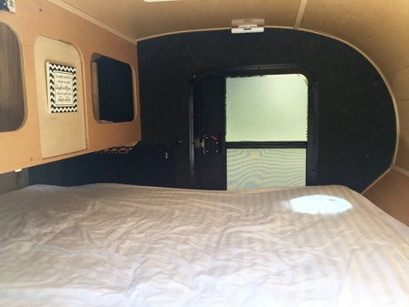 Inside a compact RV rental: a comfy bed, functional storage, a wall sign, and a rear door with a screen.