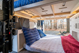 Cozy rv rental interior with bunk bed & lower bed, offering a view of autumn trees. Perfect for your next adventure!