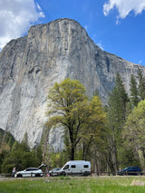 An rv rental and other vehicles parked at the base of imposing El Capitan in Yosemite Valley.