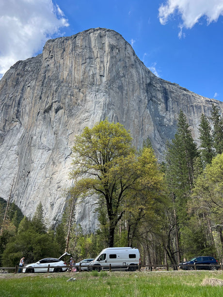 An rv rental and other vehicles parked at the base of imposing El Capitan in Yosemite Valley.