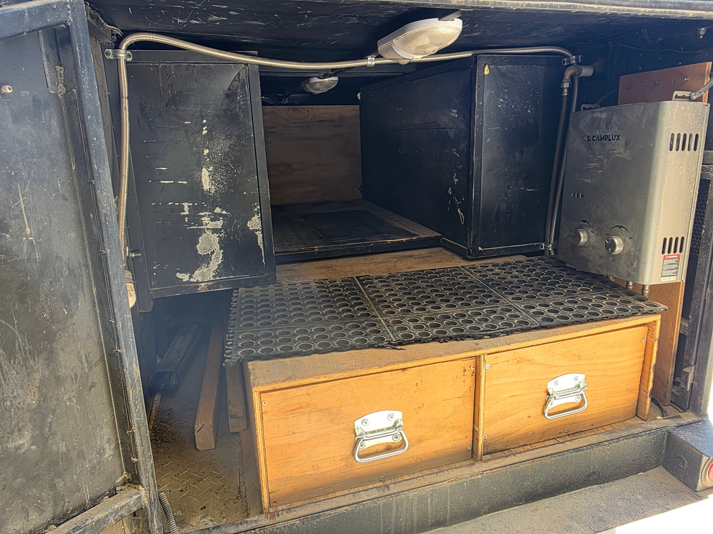 RV rental utility space with a Camplux water heater, black storage cabinets, wooden drawers, and overhead lighting. — photo 7