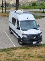 White Mercedes-Benz Sprinter camper van, ideal for RV rental, parked in a lot near green space.