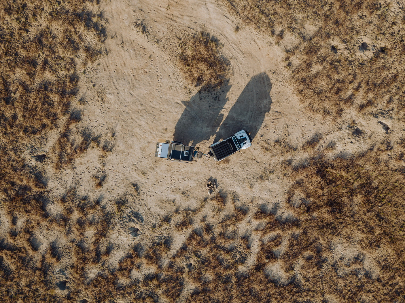 Aerial view: An RV rental and truck parked on sandy terrain with dry vegetation, ideal for remote desert camping.
