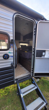 An RV rental's open door shows its interior with bed & cabinets, plus exterior steps on grass. Ready for adventure.