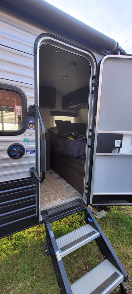 An RV rental's open door shows its interior with bed & cabinets, plus exterior steps on grass. Ready for adventure.