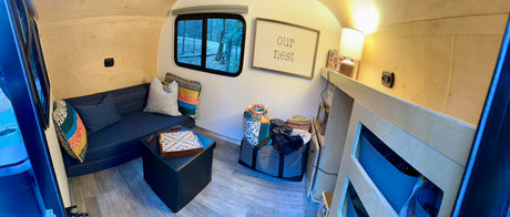 Cozy RV rental interior: sofa, Scrabble, "Our Nest" sign, and nature views through the window.