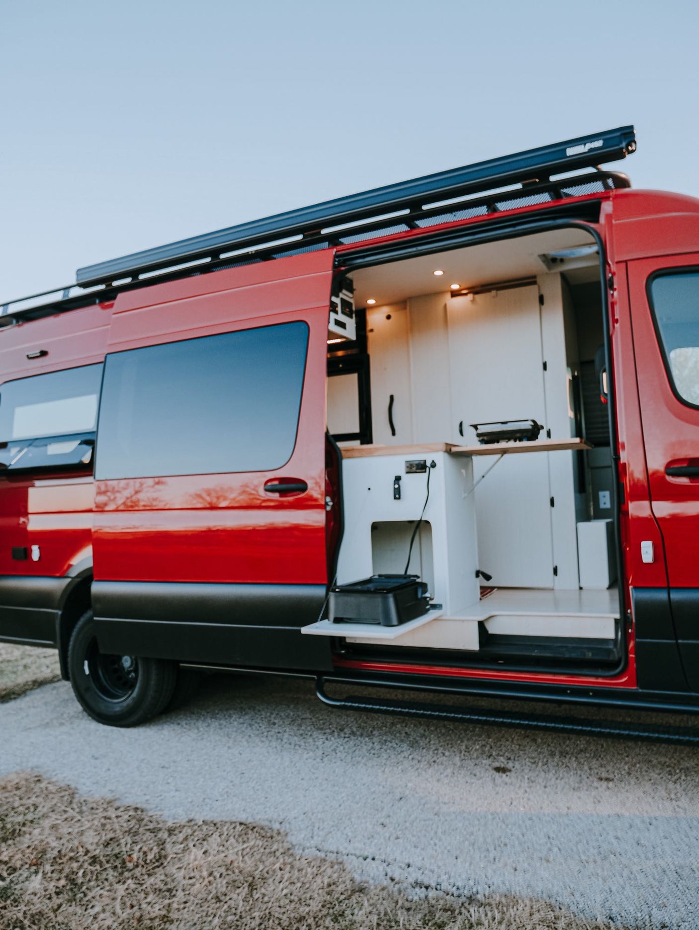 Red custom camper van with open side door reveals a functional kitchenette, ideal for RV rental adventures and outdoor cooking.