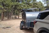 Teardrop camper RV rental and SUV parked in a pine forest campsite, ready for a nature getaway.