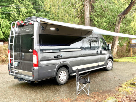 This Winnebago Travato RV rental is parked with its awning extended at a campsite, perfect for outdoor relaxation.