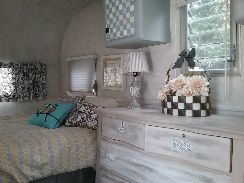 Inside a charming RV rental: a comfy bed with patterned bedding, a distressed dresser holding a lamp and floral decor. — photo 1