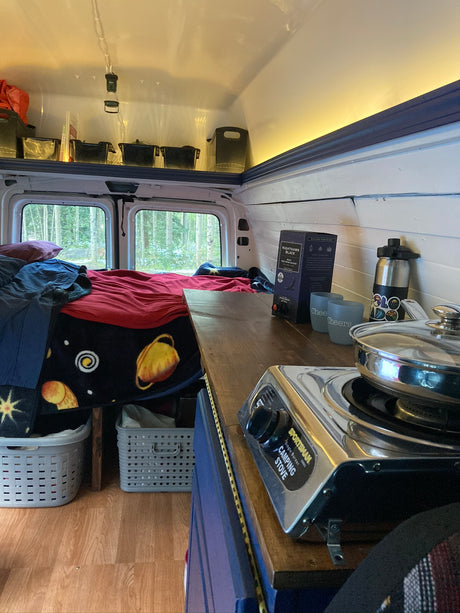 RV rental interior: cozy bed, Sportsman camping stove, Nighthawk wine, and storage for road trips.