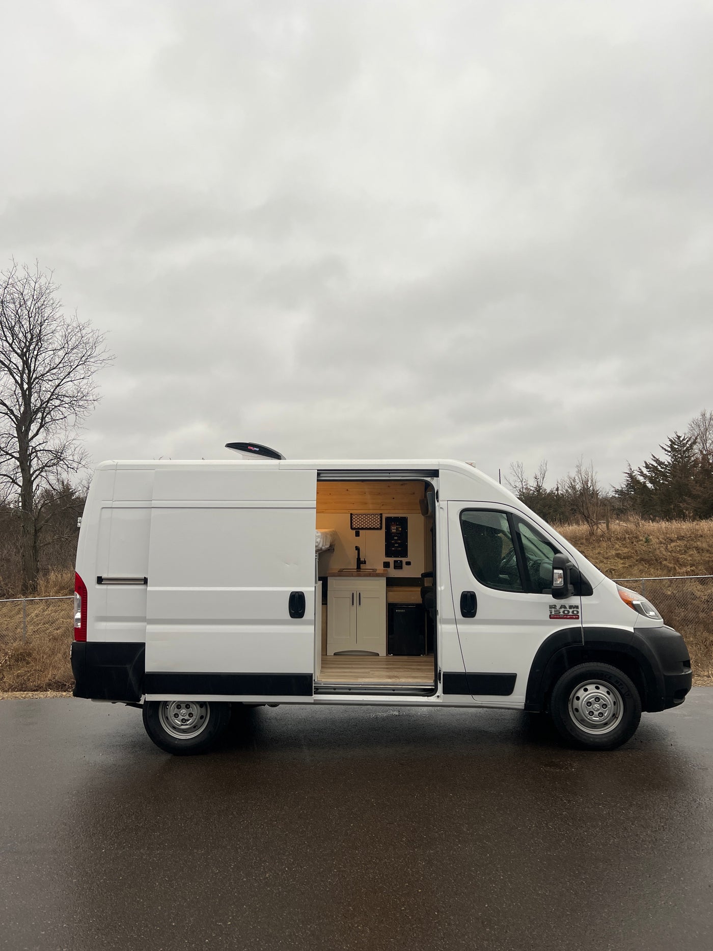 White camper van conversion with open side door revealing a custom kitchen and bed. Ideal RV rental for mobile adventures.