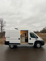 White camper van conversion with open side door revealing a custom kitchen and bed. Ideal RV rental for mobile adventures.