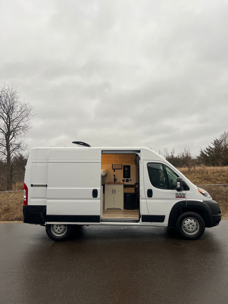White camper van conversion with open side door revealing a custom kitchen and bed. Ideal RV rental for mobile adventures.