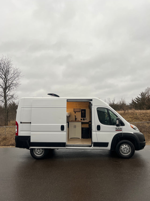 White camper van conversion with open side door revealing a custom kitchen and bed. Ideal RV rental for mobile adventures.