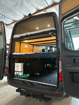 Rear view of an RV rental van's organized interior: bunk beds, a water heater, and storage for gear. Ideal for trips.
