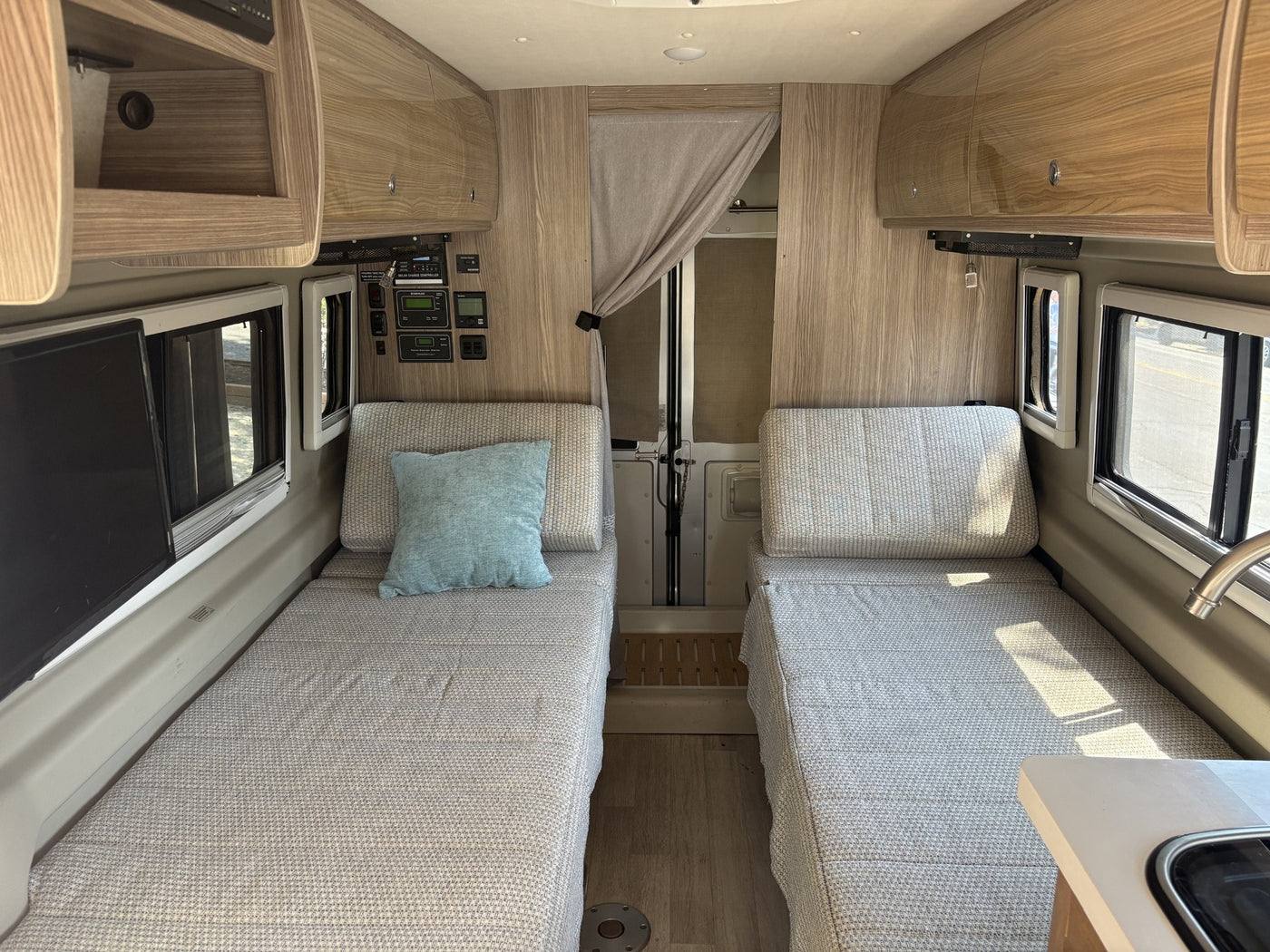 RV rental interior features twin beds with patterned bedding, overhead storage, and control panels for your journey. — photo 8