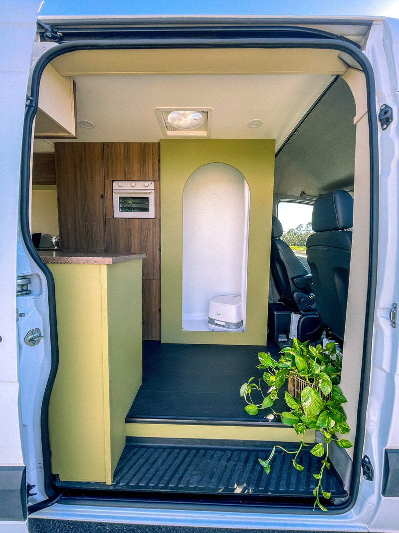 Inside a custom RV rental van: kitchenette with oven, a green arched privacy partition for the toilet, and a plant by the entrance. — photo 2