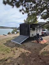 Relaxing at a scenic rv rental campsite by the lake. Travel trailer, truck, chairs, and pine trees overhead.