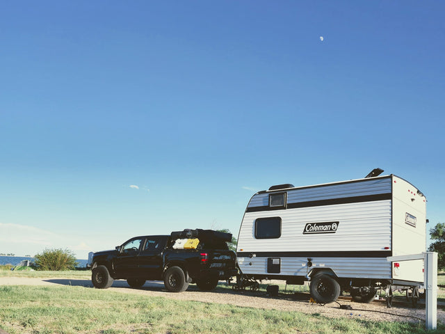 RV rental adventure: Black truck towing a Coleman travel trailer by a lake under a clear sky with a visible moon.|Silver Coleman travel trailer RV rental