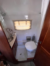 Inside an RV rental, a compact bathroom reveals a toilet, small sink, and shower setup, with a window and wood accents.