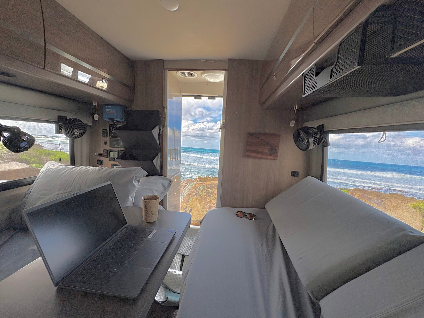 Enjoy remote work from your RV rental: a laptop setup, comfy bed, and breathtaking ocean views from the windows and door.