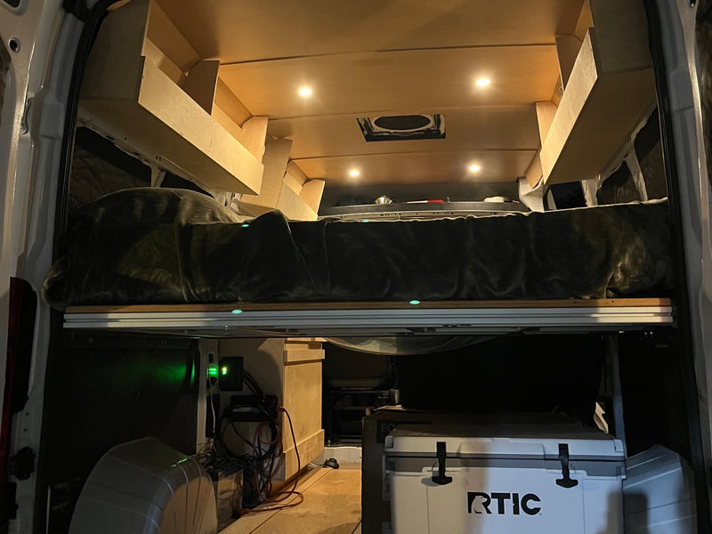  side and rear doors open to enjoy the outdoors.|Inside an rv rental: a comfy mobile office with laptop & iPad. Two dogs relax on the grass outside the open door.|This RV rental features an elevated bed — photo 4