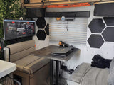 RV rental's modern interior features a dinette, TV, laptop setup, hexagonal decor, and a black dog on a comfy bed.